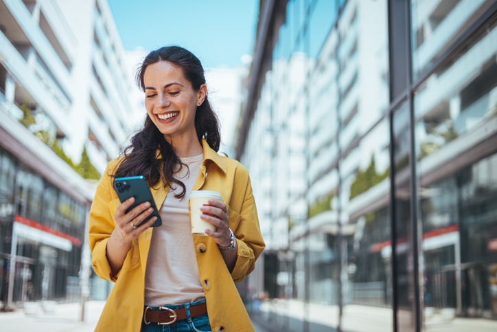 White woman using cell phone and holding coffee