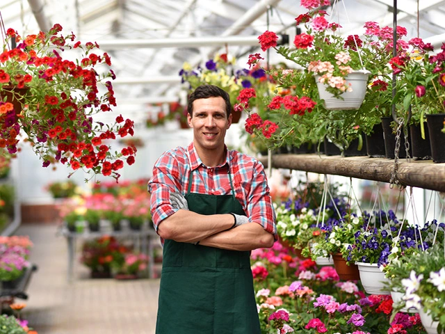 man in green apron with arms crossed standing in garden